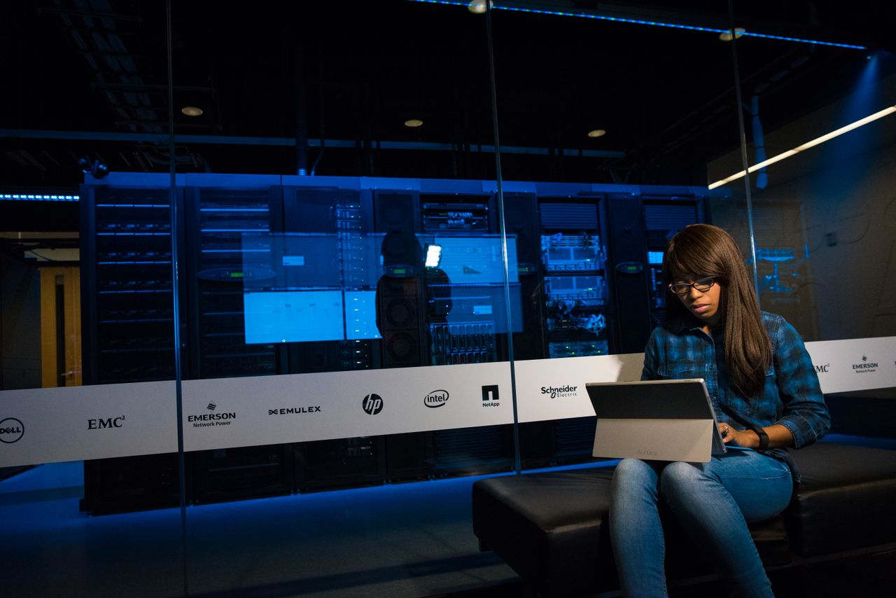 Services Woman using a laptop in a server room, showcasing modern technology and work environment.